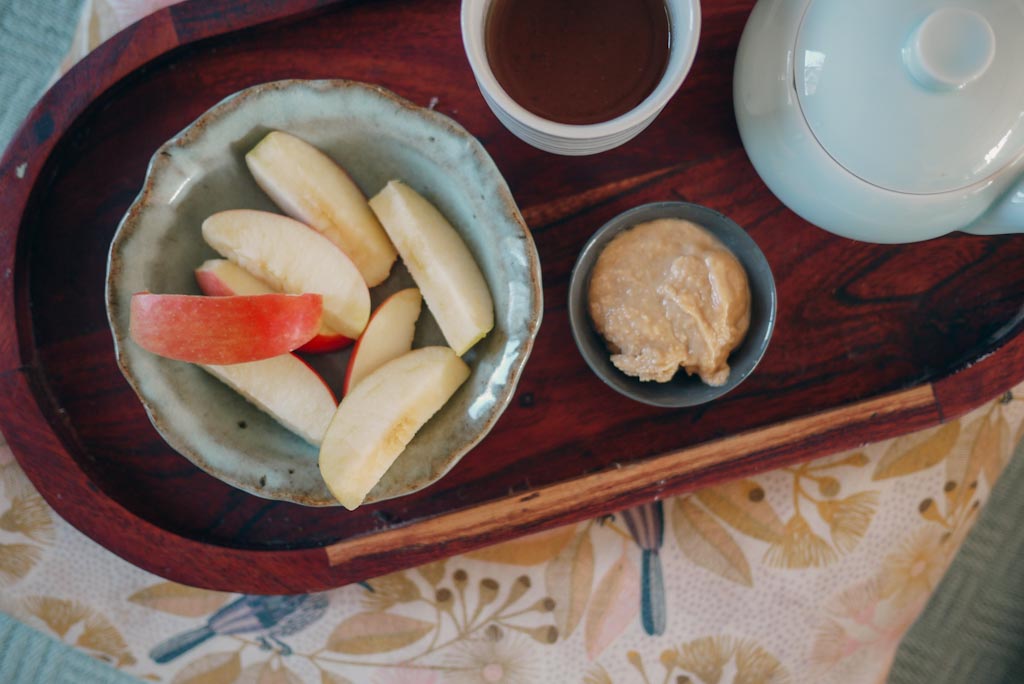 Sliced apples, peanut butter and small blue teapot and cup on wooden tray.  One of the easiest breastfeeding snacking options!