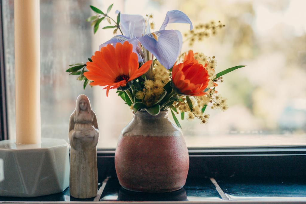 A posy of early spring flowers in the kitchen window next to a pregnant woman figurine and beeswax candle