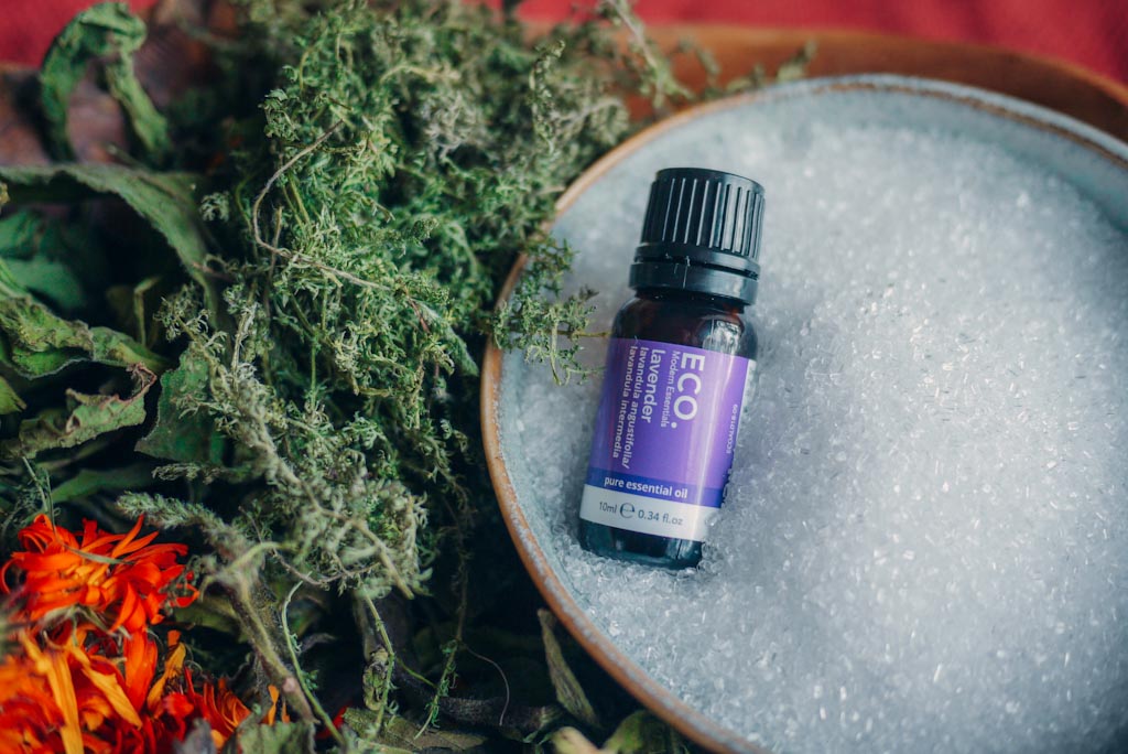 Bottle of lavender essential oil arranged in bowl of epsom salts and dried herbs