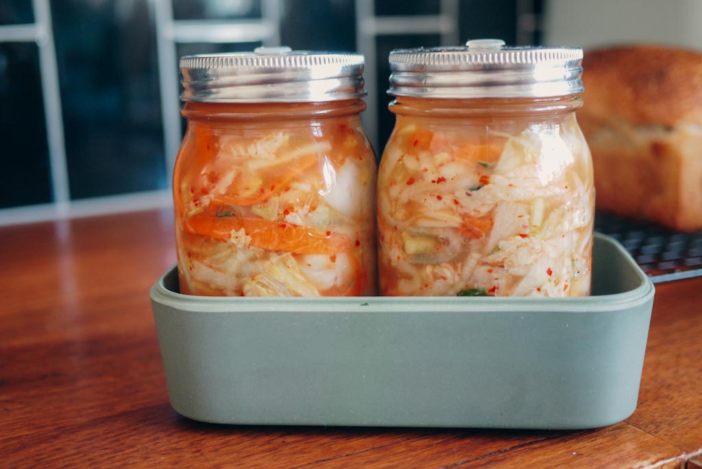Two jars of kimchi in small container to collect fermentating juices
