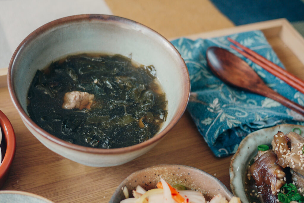 Bowl of seaweed soup on tray with other side dishes, wooden spoon and chopsticks