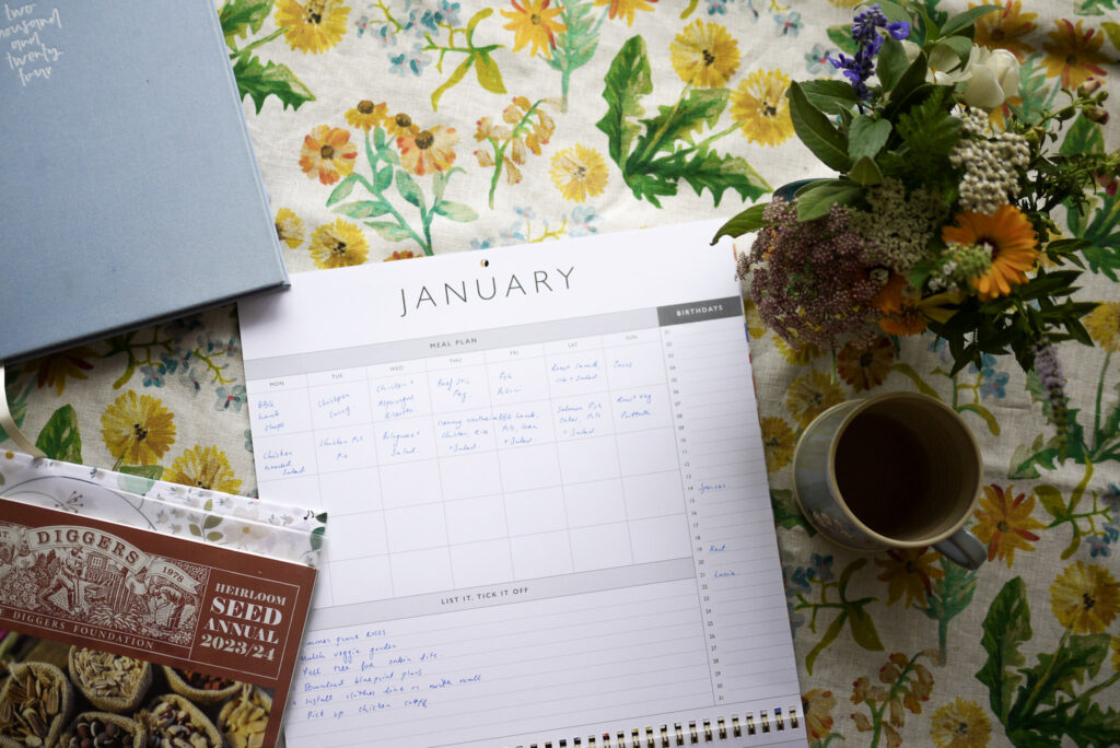 Paper calendar for January with cup of tea, flower, diary and home management system binder open